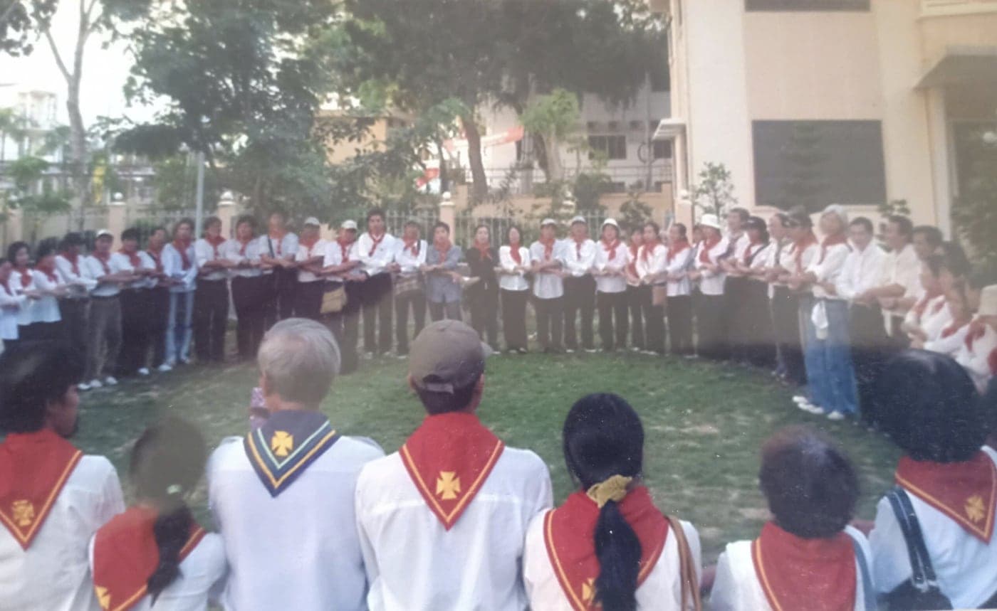 Vòng tròn sinh hoạt trong khuôn viên nhà thờ — các anh chị Huynh Trưởng mang khăn quàng đỏ, một số mang khăn Huấn Luyện Viên viền màu.